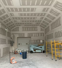 Empty construction room with unfinished drywall, scaffold, ladder, and a lift cart inside.