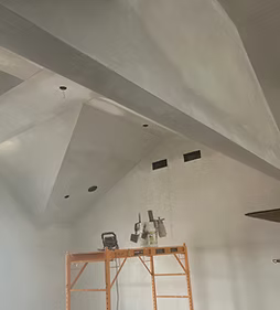 Interior room with white vaulted ceiling, recessed lights, and an orange scaffold against the wall