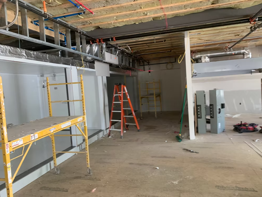 Interior construction site with scaffolding, ladders, exposed ceiling, and unfinished walls in a large room