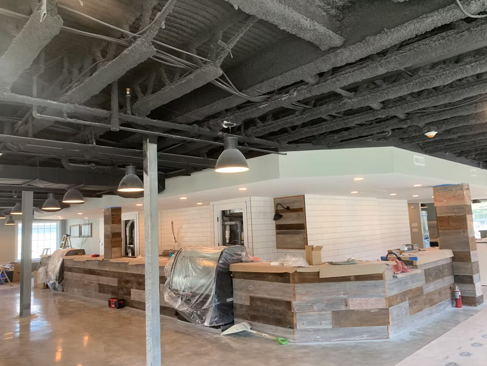 Restaurant interior with unfinished bar, exposed ceiling beams, and pendant lights
