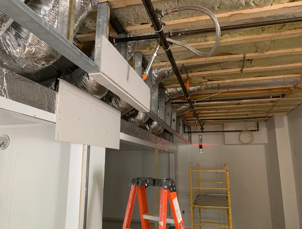 Construction site ceiling with exposed ducts, orange ladders, and yellow scaffolding in a hallway
