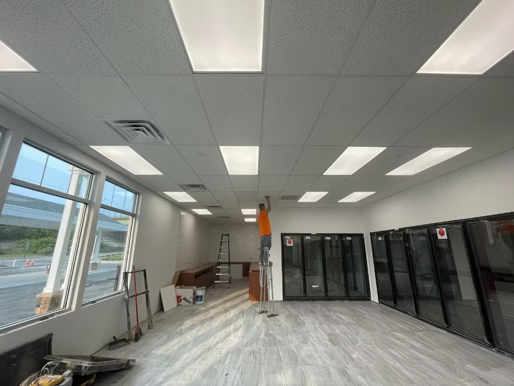 Empty office room with fluorescent lights, large windows, and dark storage cabinets along the wall