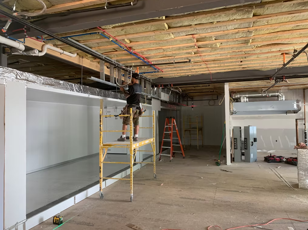 Construction worker on scaffolding in a gutted interior with exposed ceiling beams and ladders