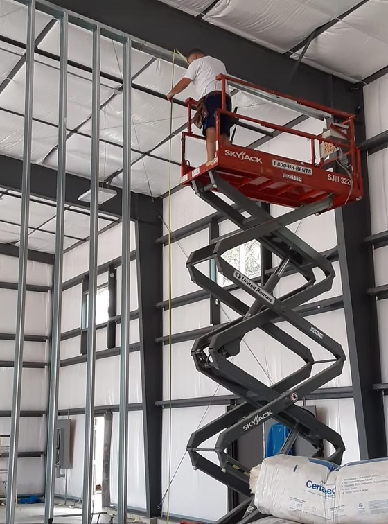 Worker on a red scissor lift installing framing inside a metal building under construction