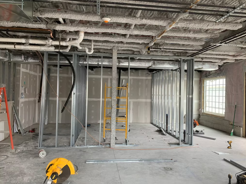 Interior under renovation with metal framing, ladders, exposed ceiling, and construction tools on the floor.