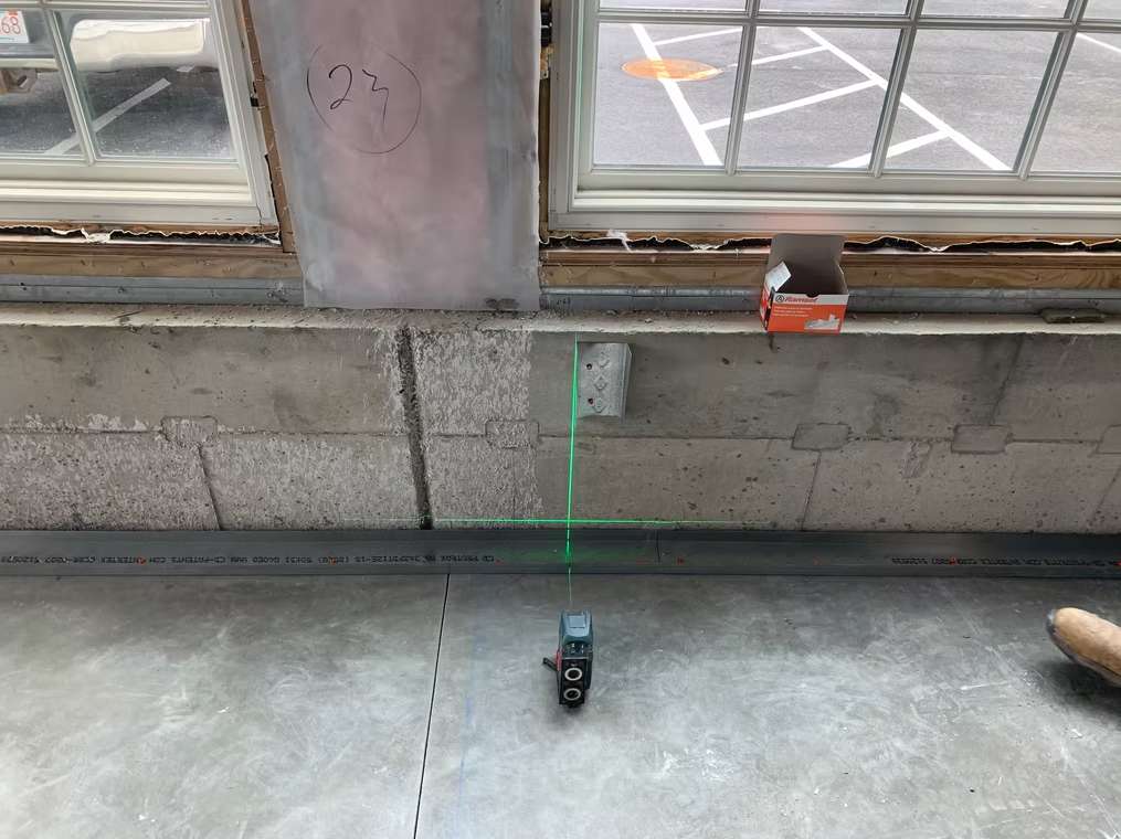 Laser level projecting a green line on a concrete floor beneath windows indoors