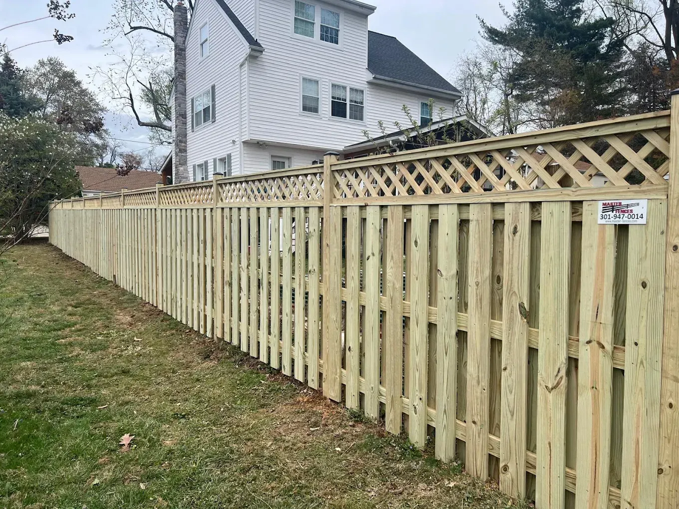 New wooden privacy fence along a grassy yard beside a white house