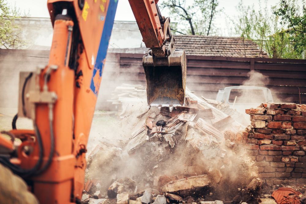 Orange Excavator Demolishing a Brick Building, Creating Dust and Debris — Mareeba Crane Hire In Atherton, QLD