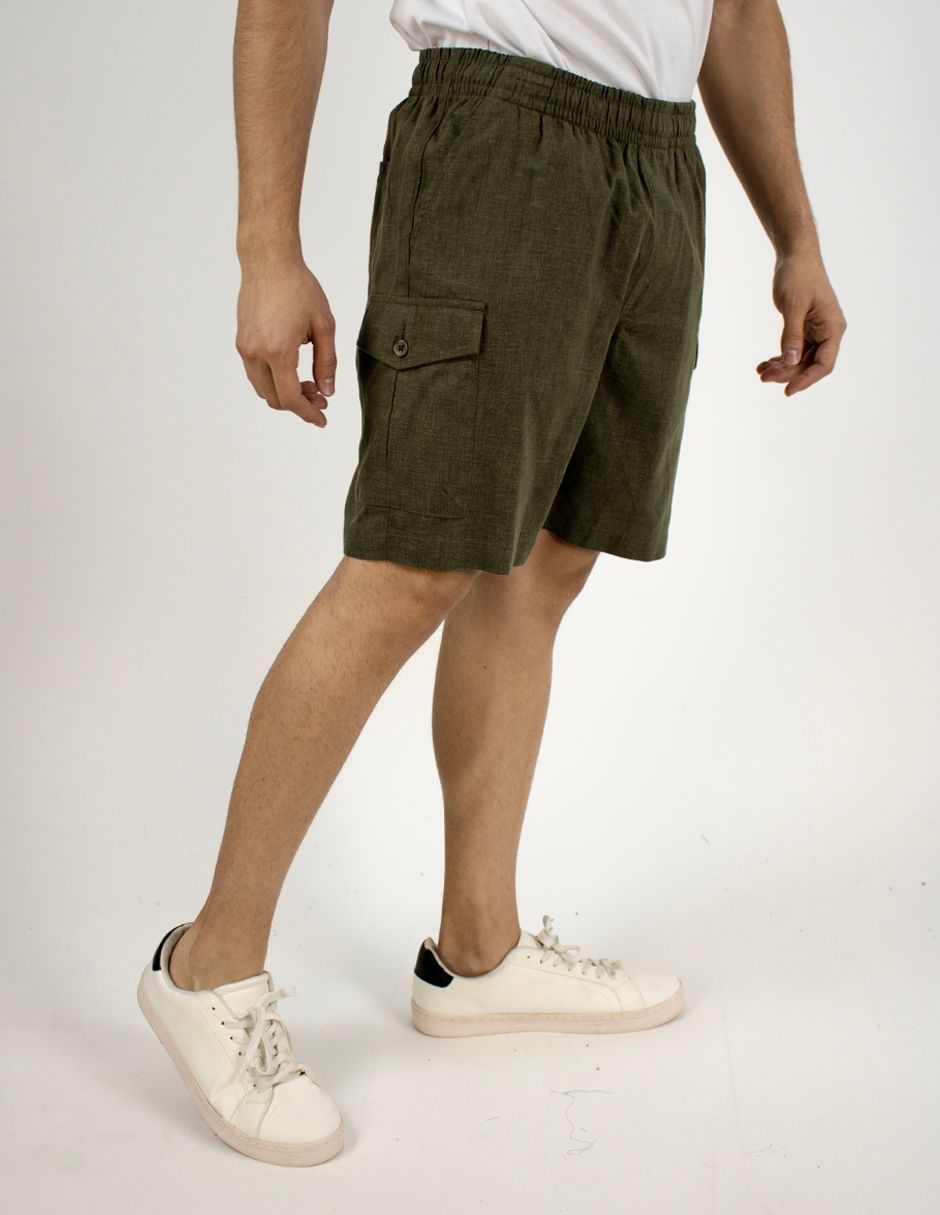 Persona con pantalones cortos cargo color oliva, camiseta blanca y zapatillas blancas, de pie sobre un fondo liso.