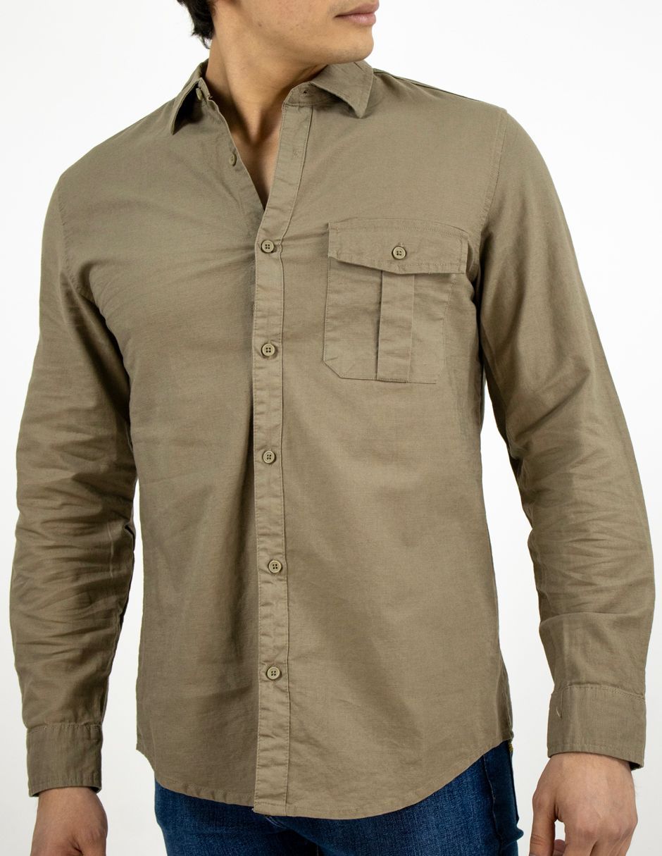 Hombre con camisa de manga larga color canela abotonada con bolsillo en el pecho y vaqueros azules, de pie sobre un fondo blanco.