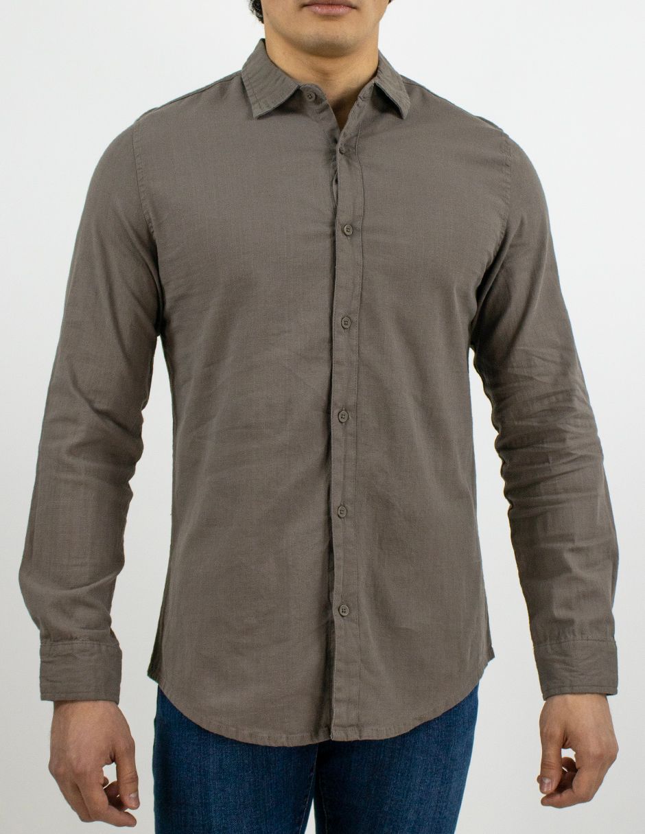 Hombre con camisa gris abotonada y vaqueros azules sobre un fondo blanco liso.