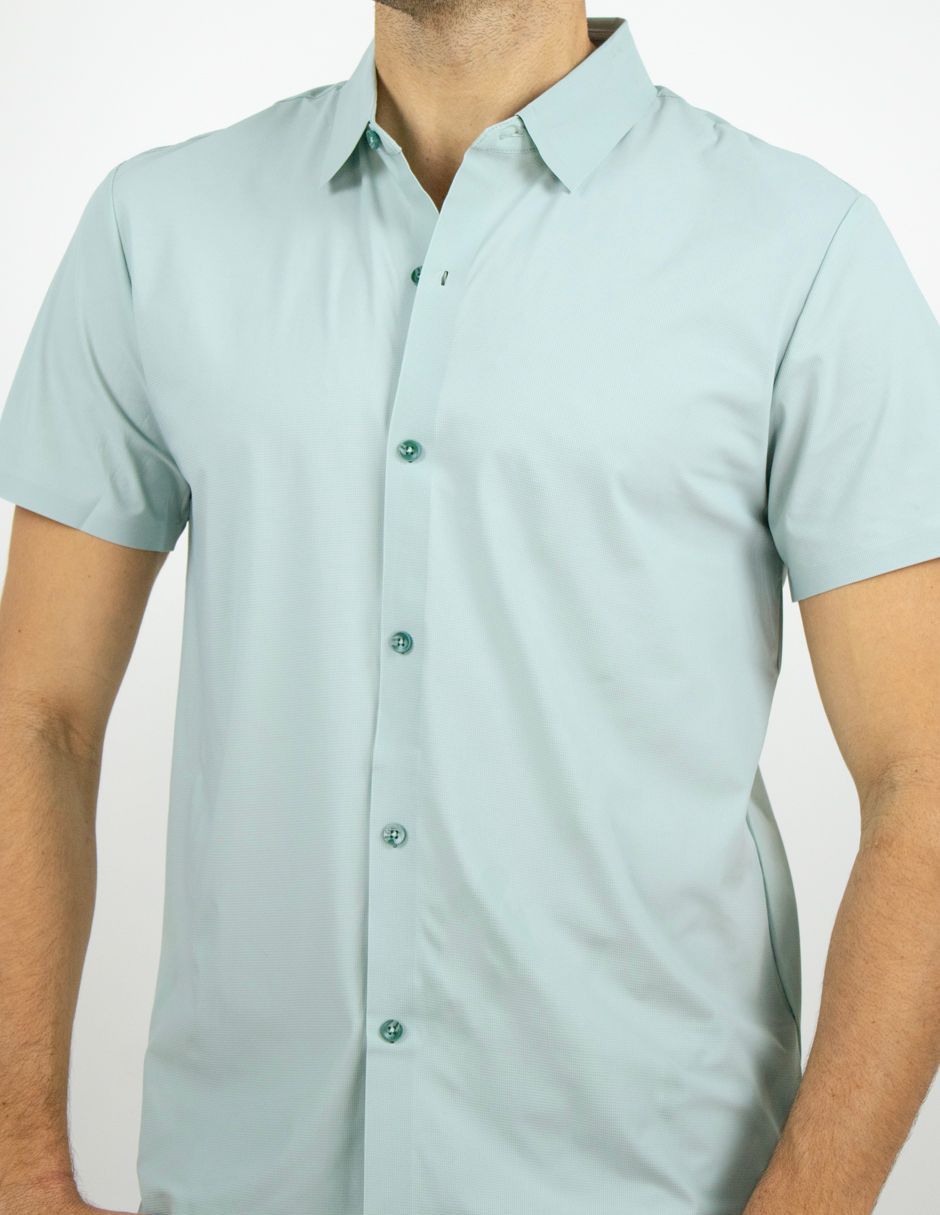 Camisa azul claro de manga corta con botones sobre una persona, sobre un fondo blanco liso.