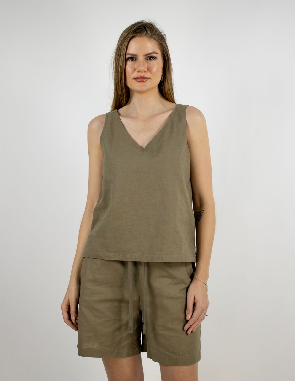 Mujer de pie con top sin mangas color oliva y pantalones cortos a juego sobre un fondo liso.