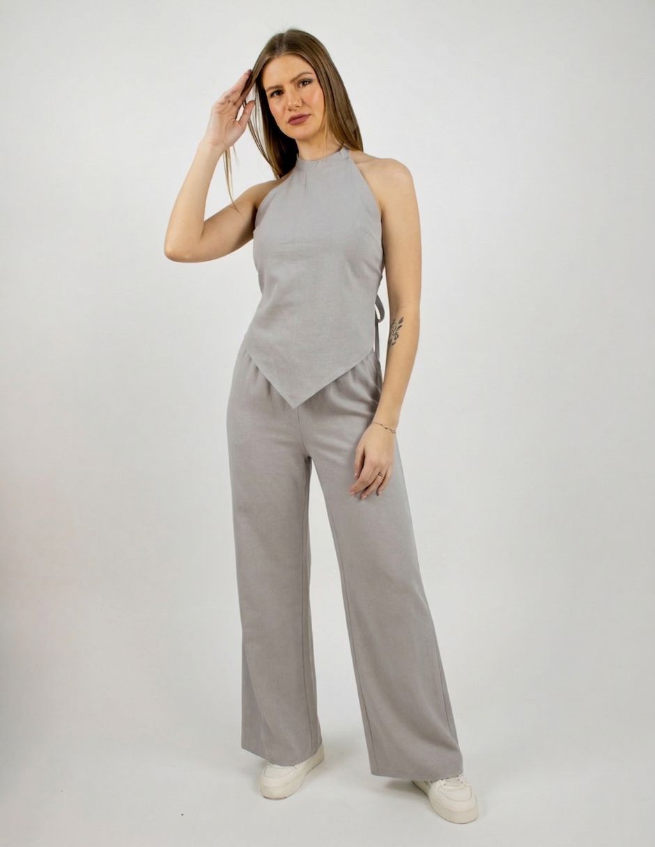 Persona con un top gris sin mangas y pantalones anchos de pie sobre un fondo blanco.