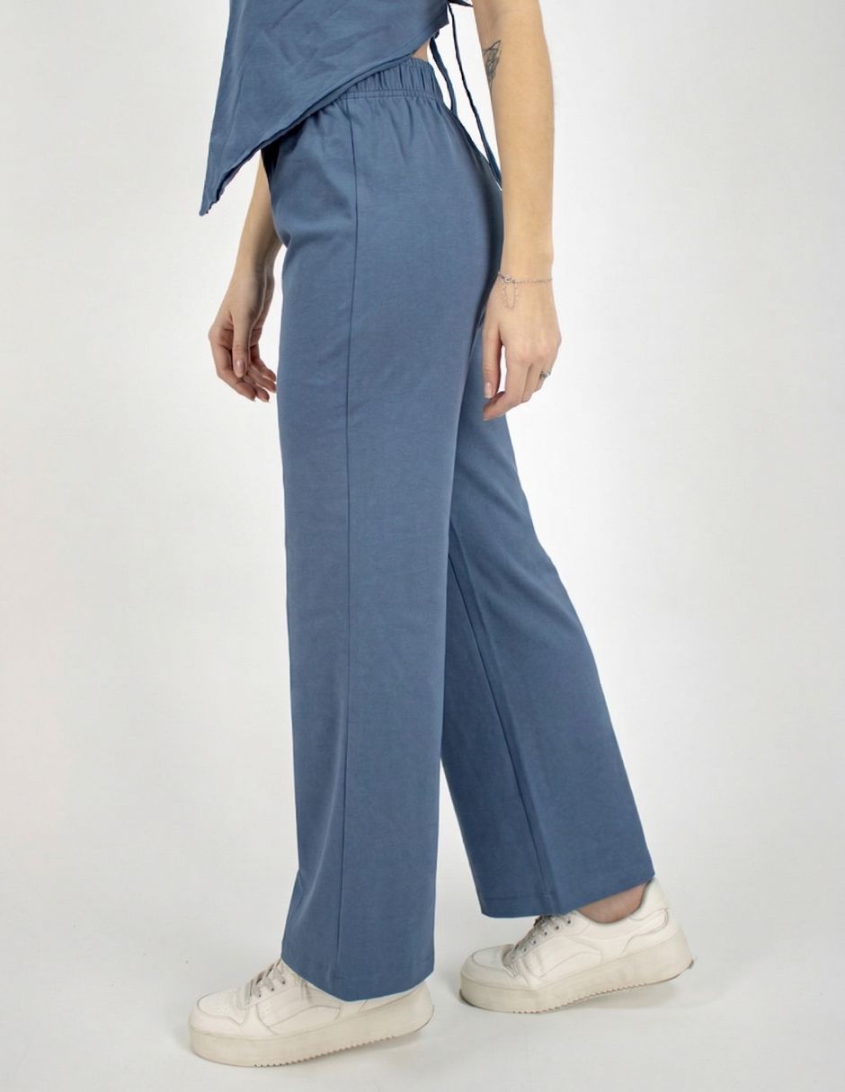 Persona vestida con pantalones anchos azules y zapatillas blancas, de pie de perfil.