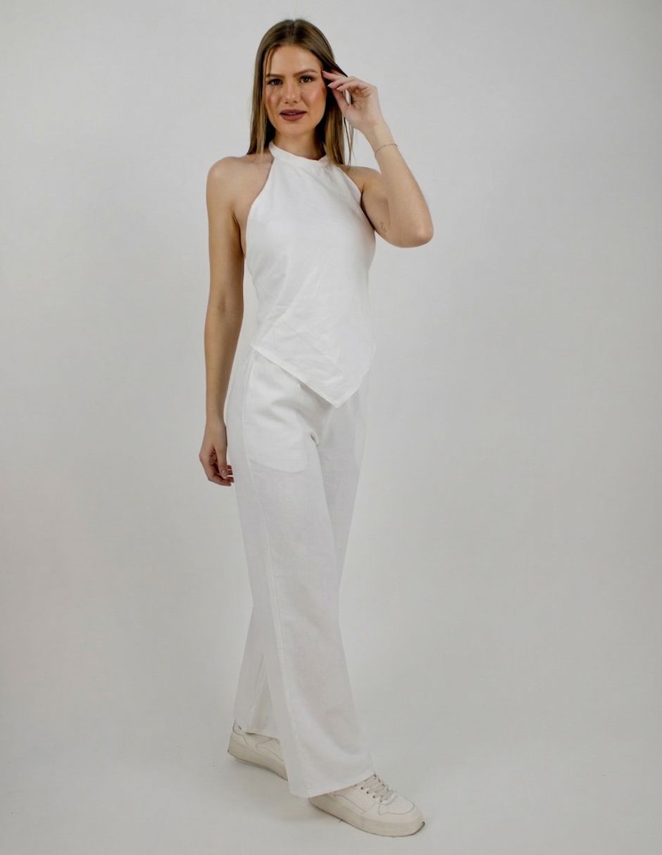 Mujer con top blanco sin tirantes y pantalones, de pie sobre un fondo gris liso.