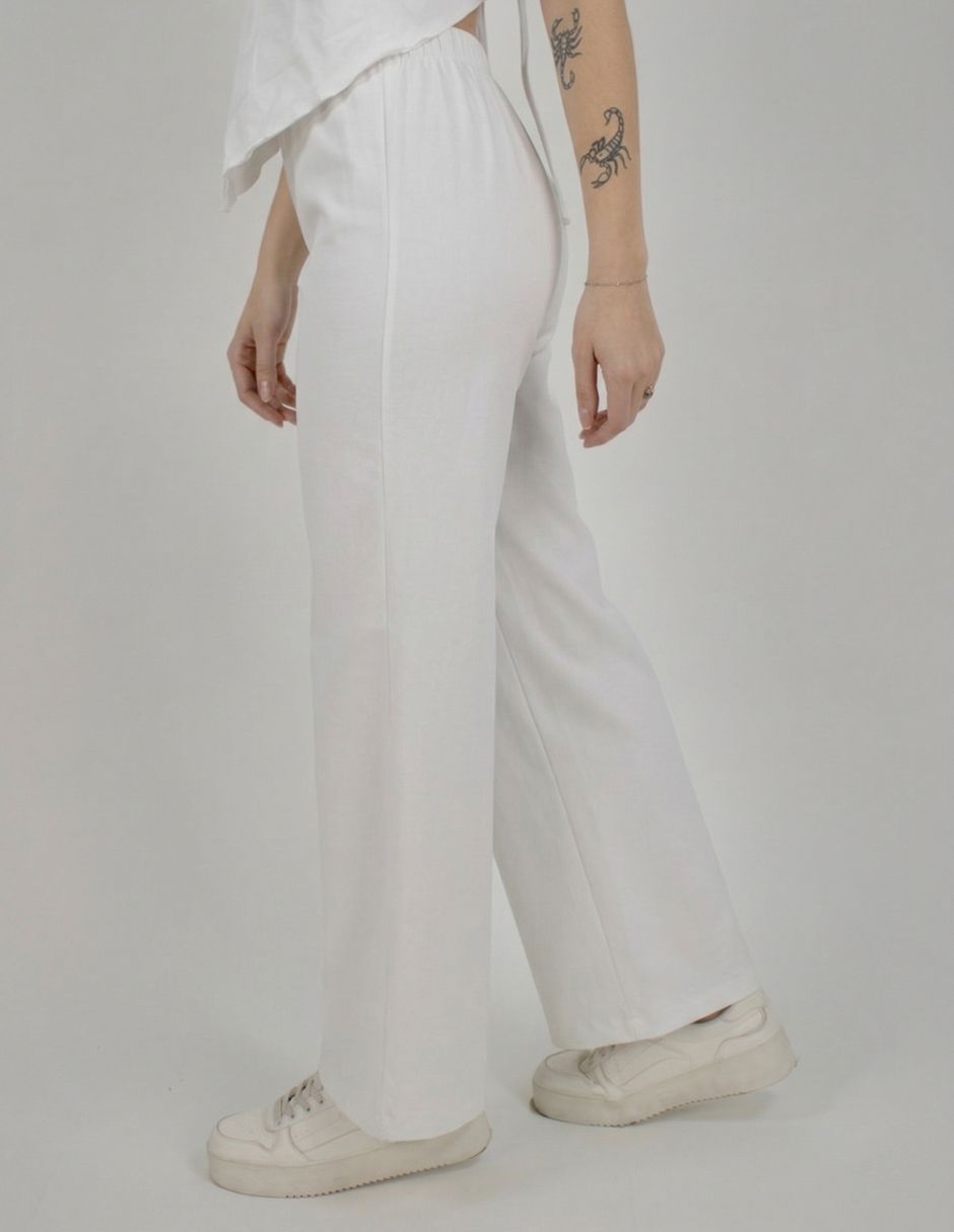 Persona vestida con pantalones blancos y zapatillas deportivas, de perfil contra un fondo liso.