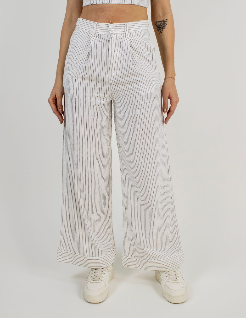 Persona con pantalones anchos de rayas blancas y zapatillas blancas sobre un fondo liso.