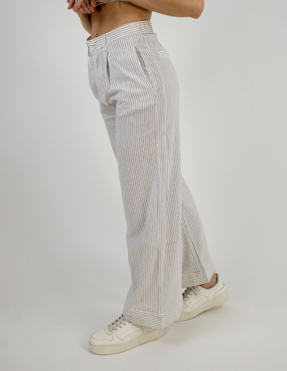 Persona con pantalones anchos de rayas blancas y zapatillas blancas en un estudio.