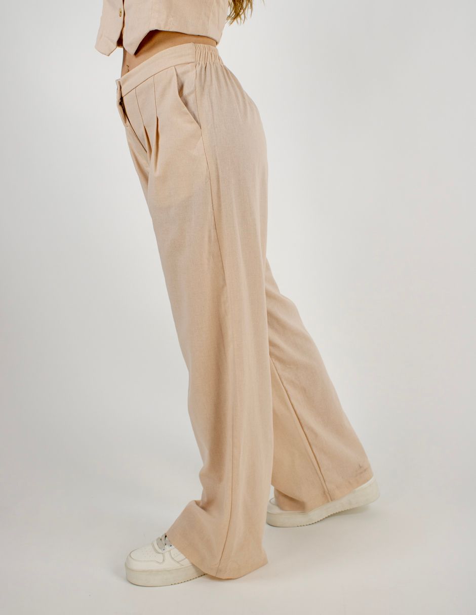 Pantalones anchos de color beige con pliegues, mostrados en una persona de pie sobre un fondo liso.