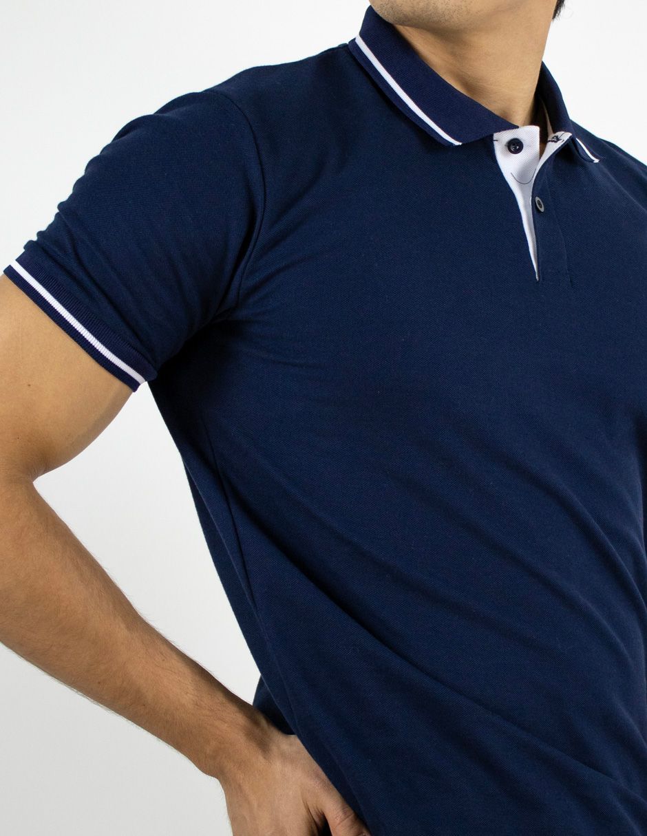 Polo azul marino con ribetes blancos en el cuello y las mangas, mostrado en una persona sobre un fondo blanco.
