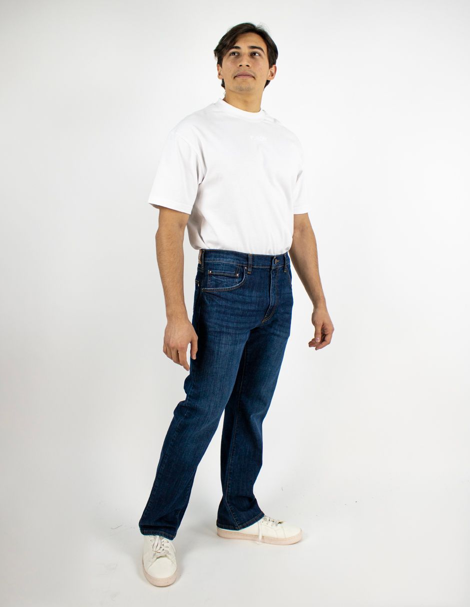 Hombre con camiseta blanca y vaqueros de pie sobre un fondo blanco liso.