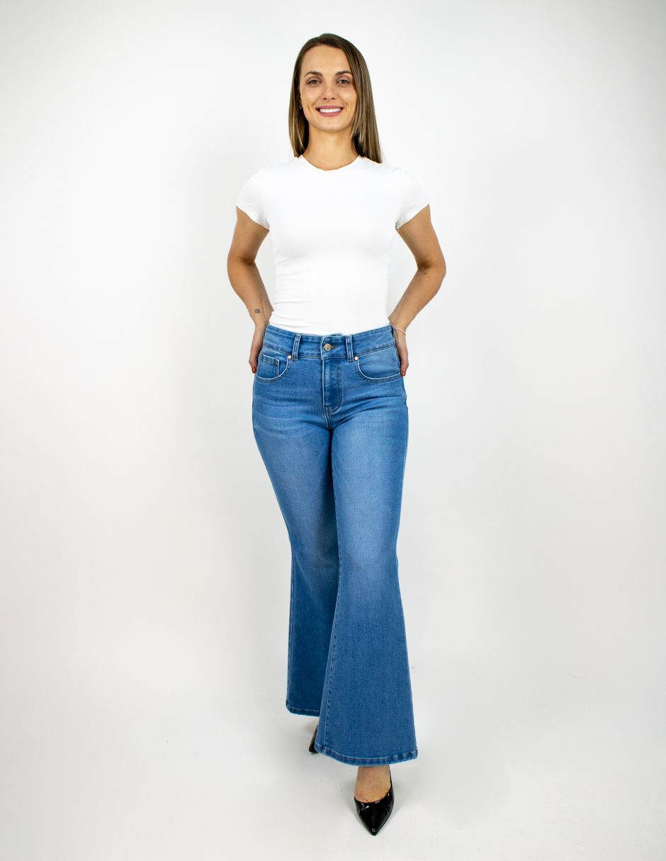 Persona con camiseta blanca y vaqueros azules acampanados de pie sobre un fondo blanco liso.