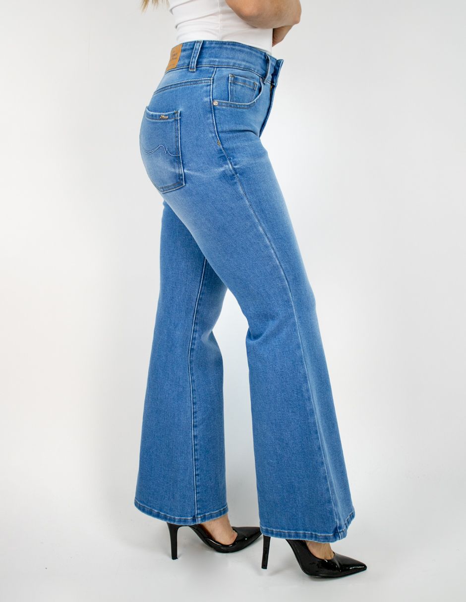 Mujer con pantalones vaqueros acampanados azules y tacones negros, vista de perfil sobre un fondo blanco.