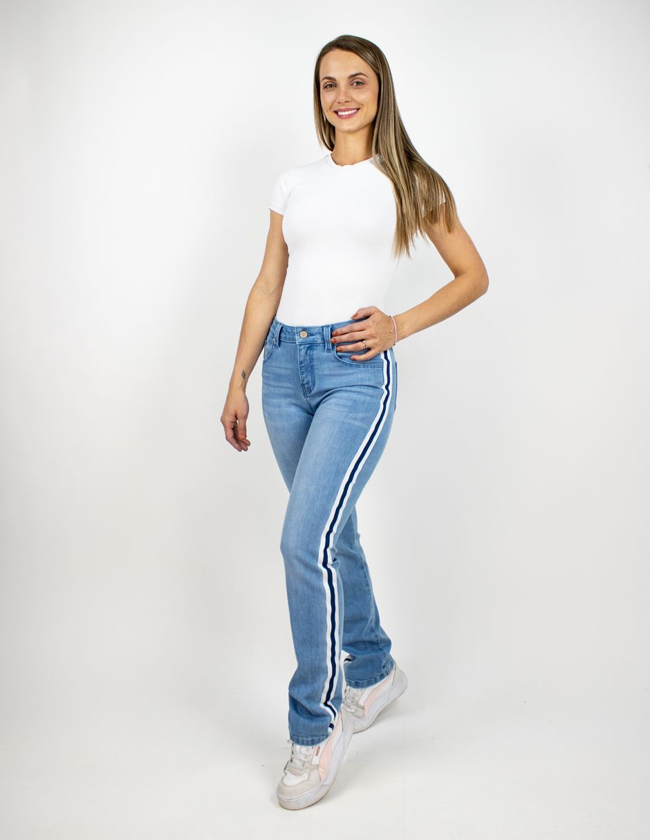 Mujer de pie con una blusa blanca y vaqueros azul claro sobre un fondo blanco liso.