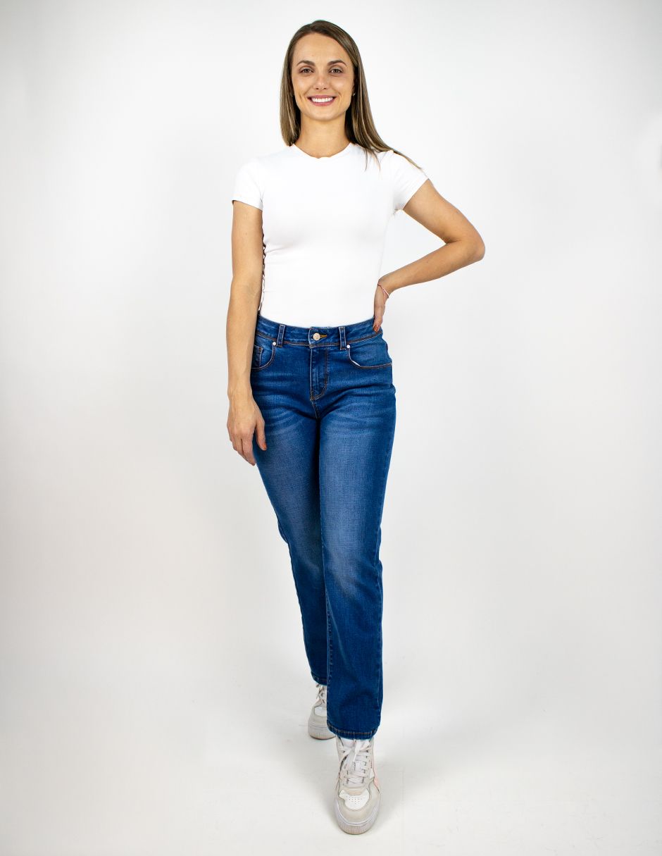 Mujer con camiseta blanca y vaqueros azules posando sobre un fondo blanco.