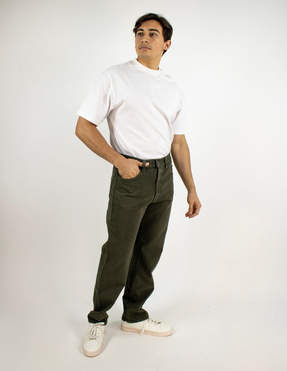 Persona de pie sobre un fondo blanco, vestida con una camisa blanca, pantalones oscuros y zapatillas blancas.