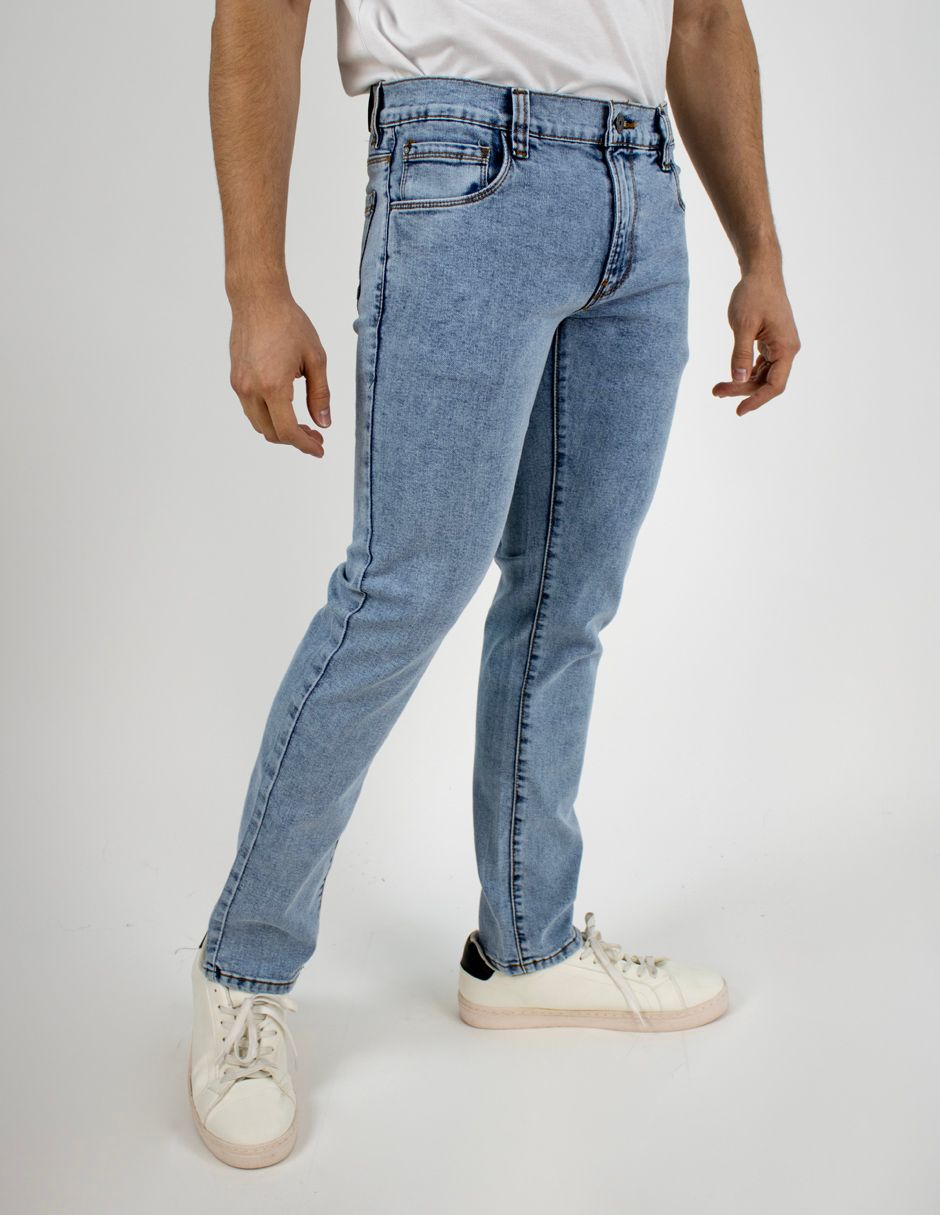 Persona vestida con vaqueros azul claro y zapatillas blancas, de pie frente a un fondo liso.