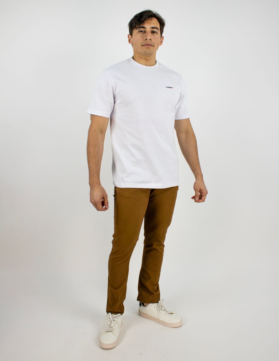 Persona de pie sobre un fondo blanco, vestida con una camiseta blanca, pantalones marrones y zapatillas blancas.