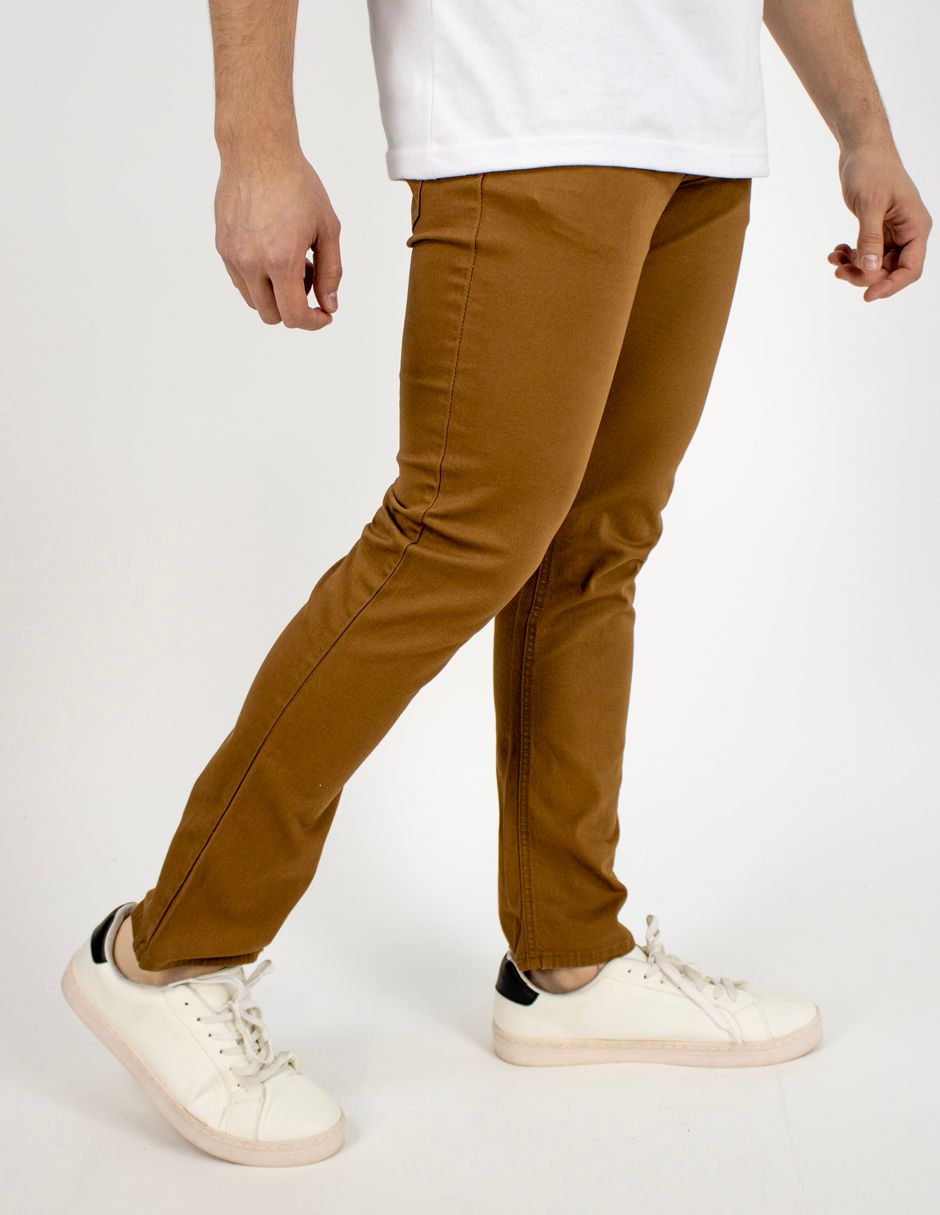 Persona con pantalones marrones y zapatillas blancas de pie sobre un fondo blanco liso.