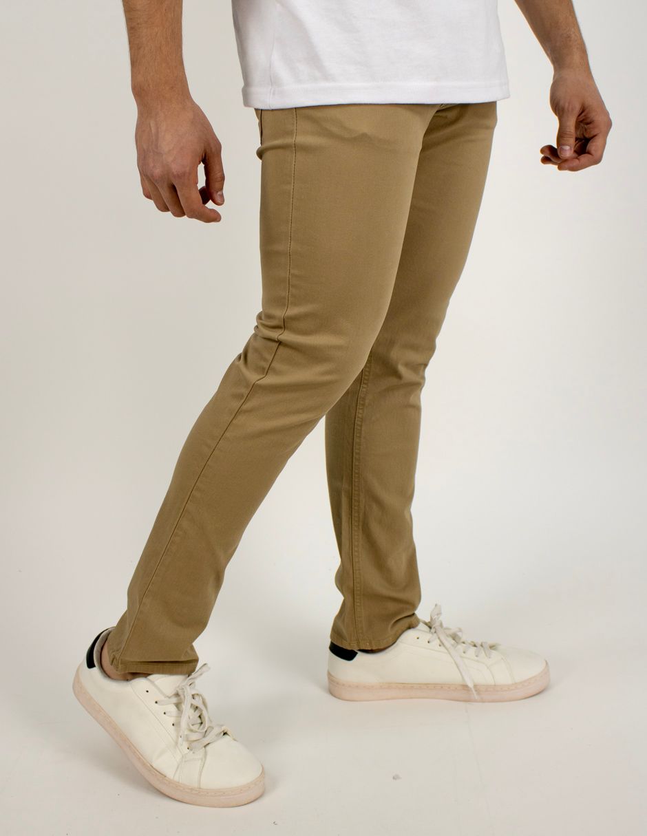 Persona con pantalones color canela y zapatillas blancas de pie sobre un fondo liso.