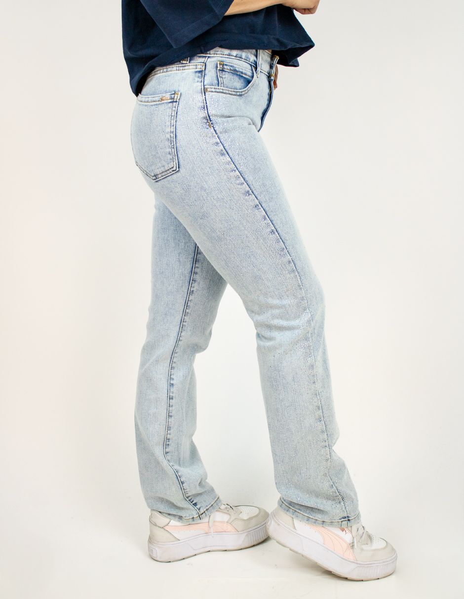 Persona vestida con vaqueros azul claro y zapatillas blancas, de perfil contra un fondo liso.