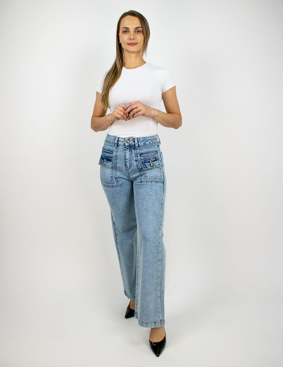 Mujer con blusa blanca y vaqueros azul claro de pie sobre un fondo blanco liso.
