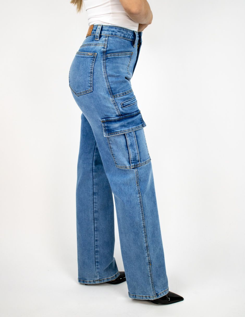 Persona con pantalones vaqueros cargo azules y zapatos negros, vista de perfil sobre un fondo blanco.
