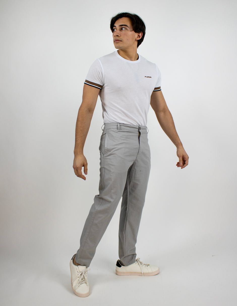 Hombre con camiseta blanca, pantalón gris y zapatillas blancas de pie sobre un fondo blanco liso.