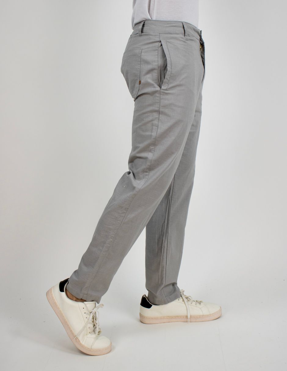 Vista lateral de pantalones grises con zapatillas blancas en una persona de pie sobre un fondo claro.