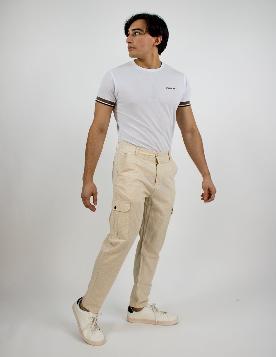 Persona de pie con camiseta blanca, pantalones cargo beige y zapatillas blancas frente a un fondo de estudio liso.