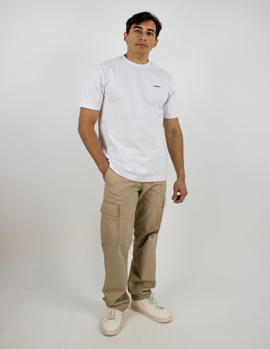 Hombre de pie sobre un fondo blanco, vistiendo una camiseta blanca, pantalones cargo beige y zapatillas blancas.