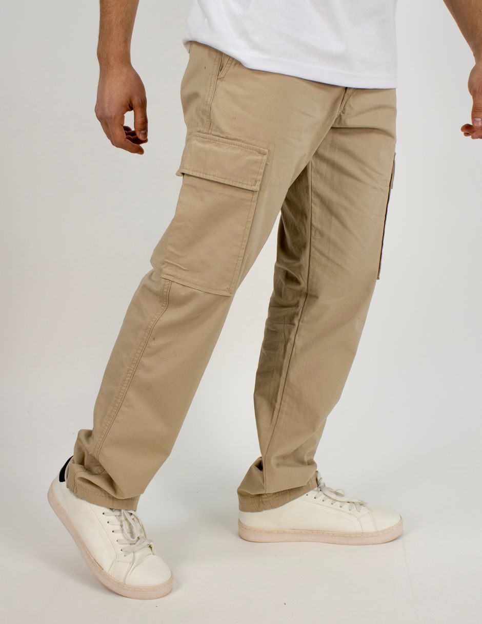 Persona con pantalones cargo color canela y zapatillas blancas de pie sobre un fondo liso.