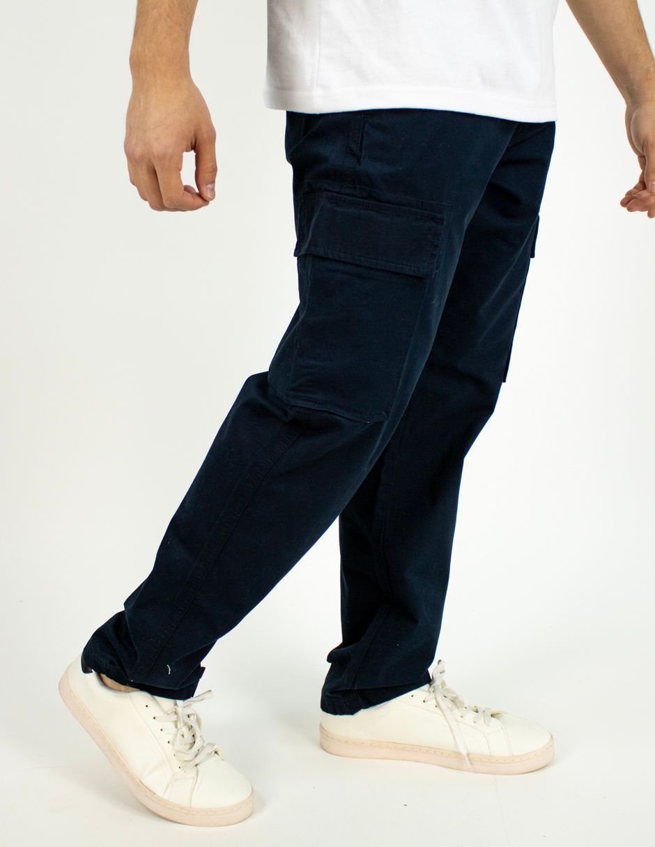 Persona con pantalones azul marino y zapatillas blancas caminando sobre un fondo blanco liso.