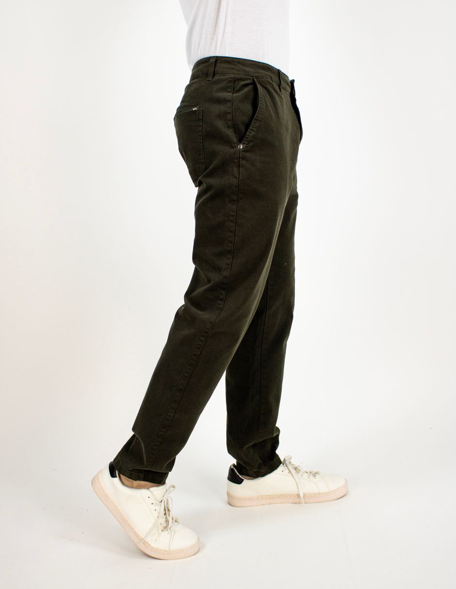 Vista lateral de una persona que lleva pantalones verde oliva oscuro y zapatillas blancas, de pie sobre un fondo blanco liso.