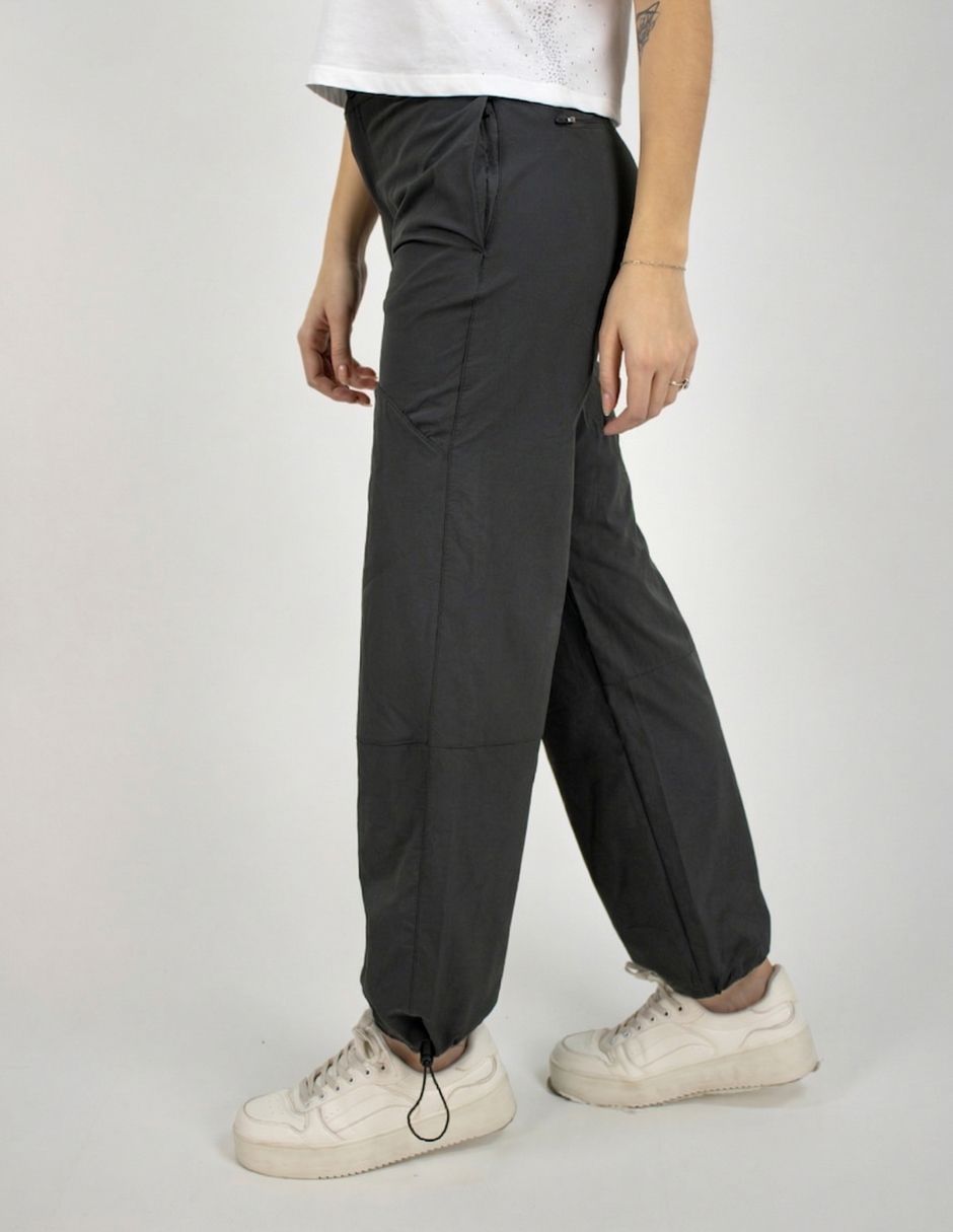 Persona con pantalones negros y zapatillas blancas de pie en un estudio frente a un fondo liso.