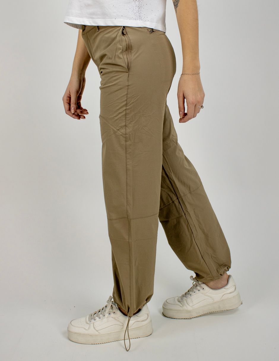 Persona con pantalones cargo color oliva y zapatillas blancas, de pie y caminando sobre un fondo liso.