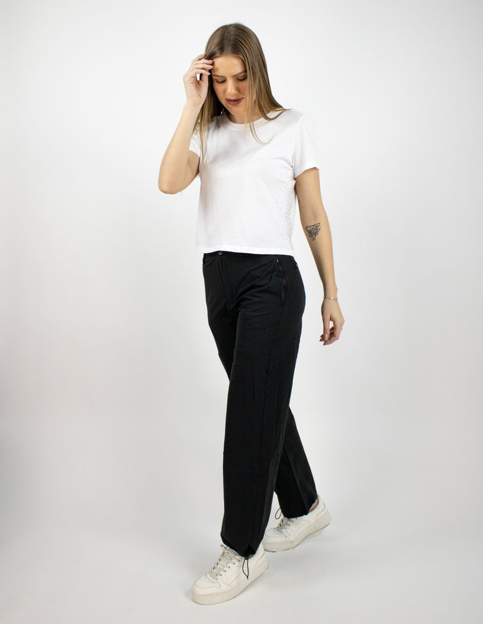 Mujer con camiseta blanca y pantalones negros caminando sobre un fondo blanco liso.