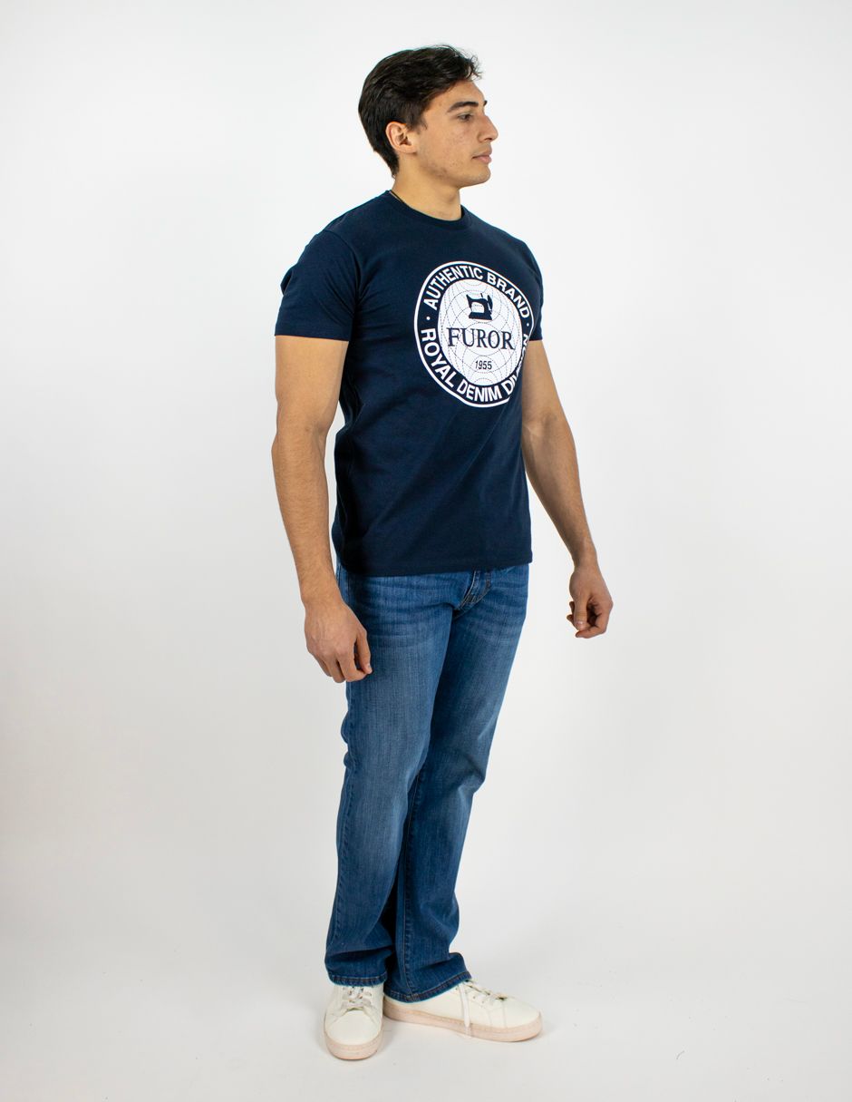 Hombre de pie con camiseta azul marino, vaqueros y zapatillas blancas sobre un fondo blanco liso.