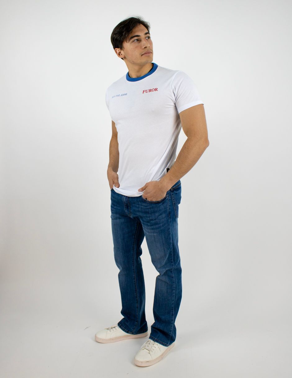 Hombre de pie con camiseta blanca y vaqueros azules sobre un fondo blanco liso.